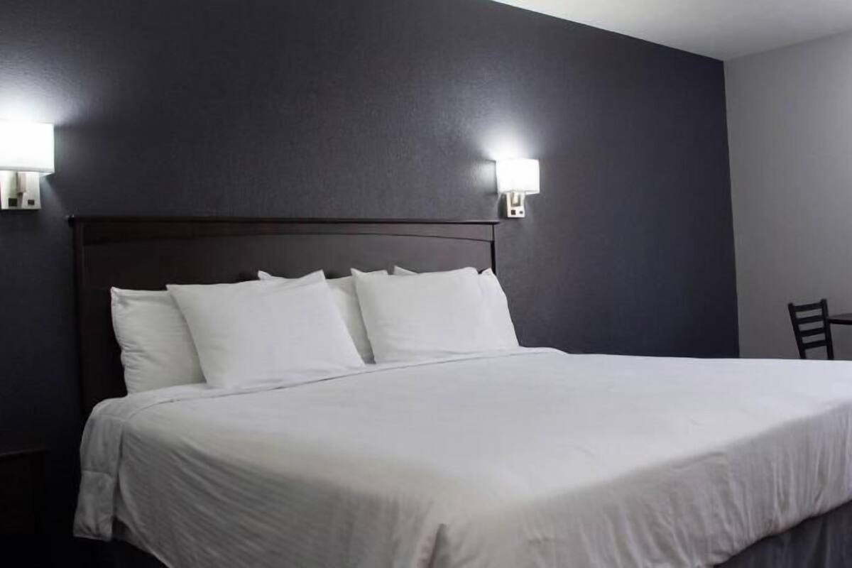 A hotel room with a large bed, two wall-mounted lights, a small table, and two chairs.