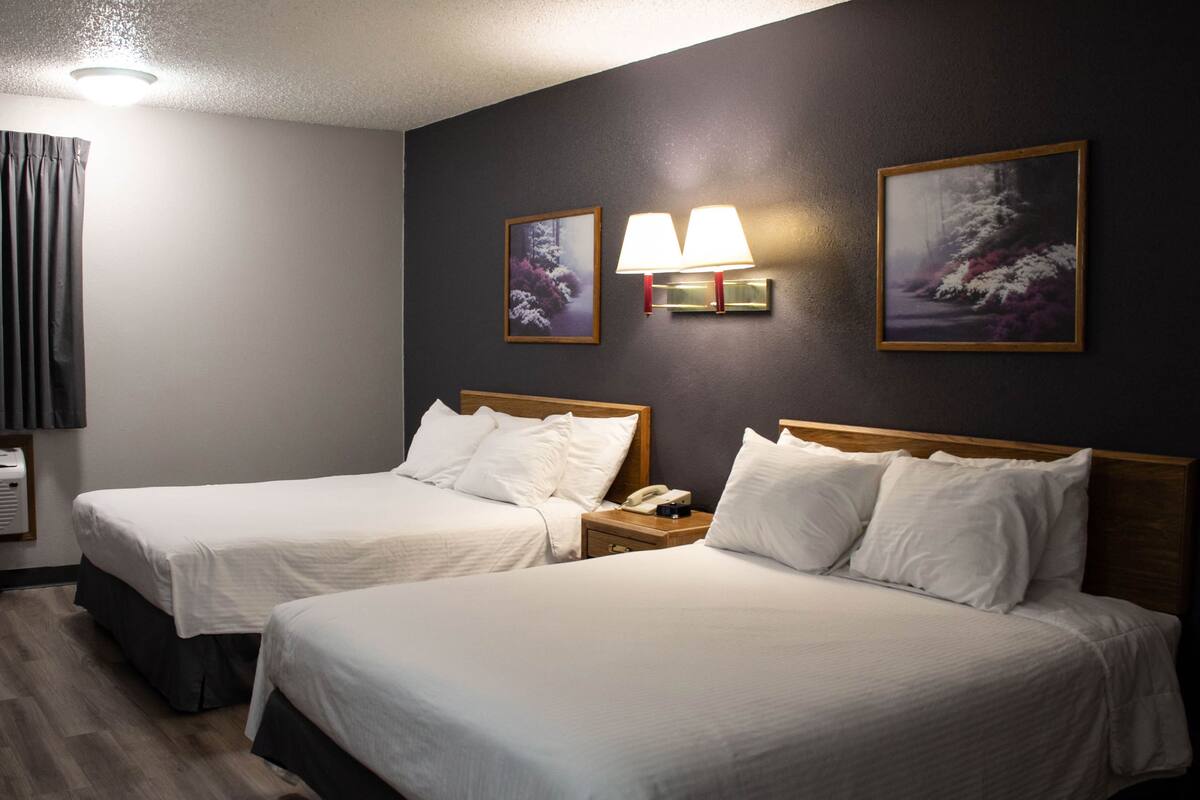 A hotel room with two beds, a nightstand with a phone, and wall-mounted lamps.