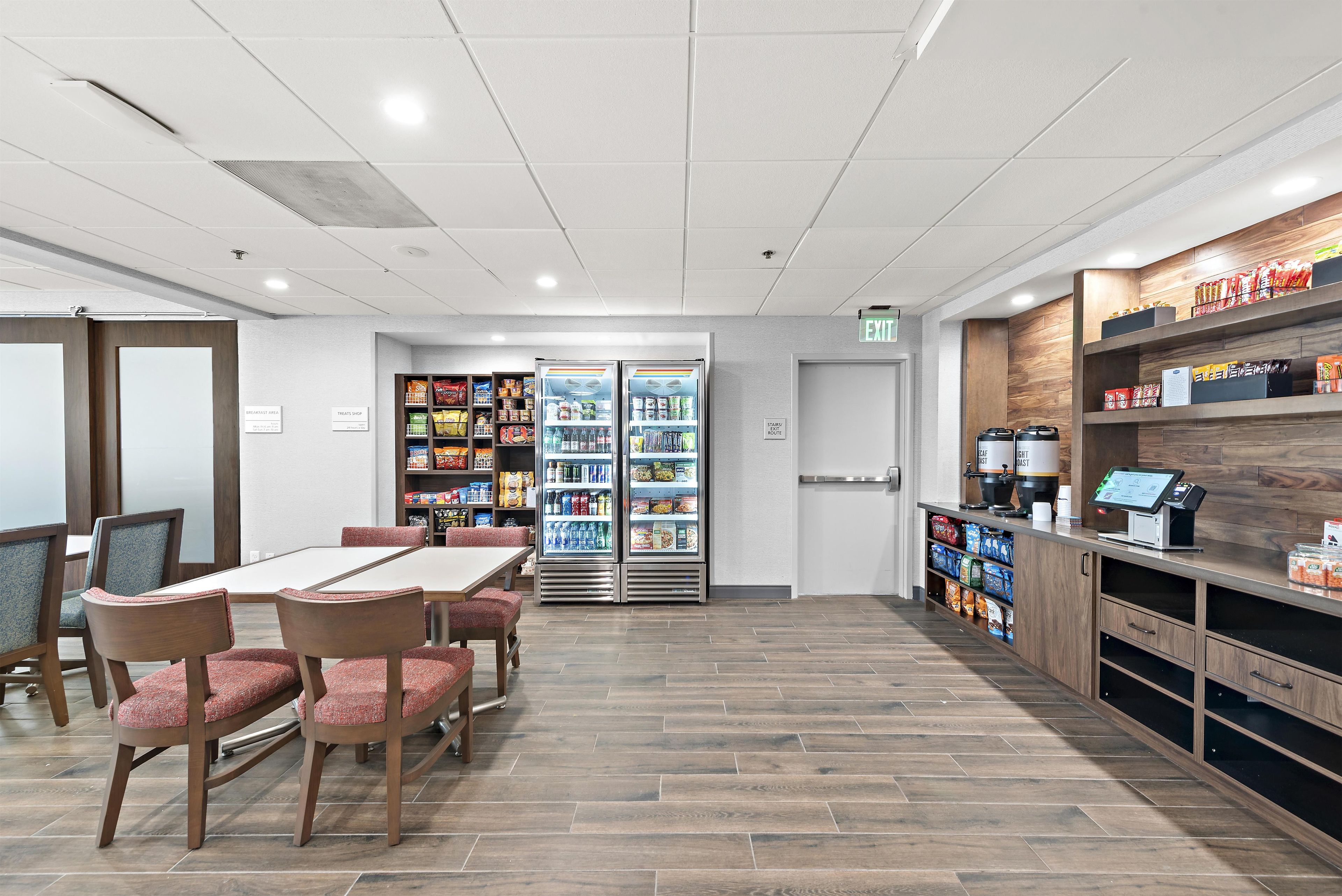 A dining area with a table and chairs, a refrigerator stocked with beverages, and shelves with packaged goods.