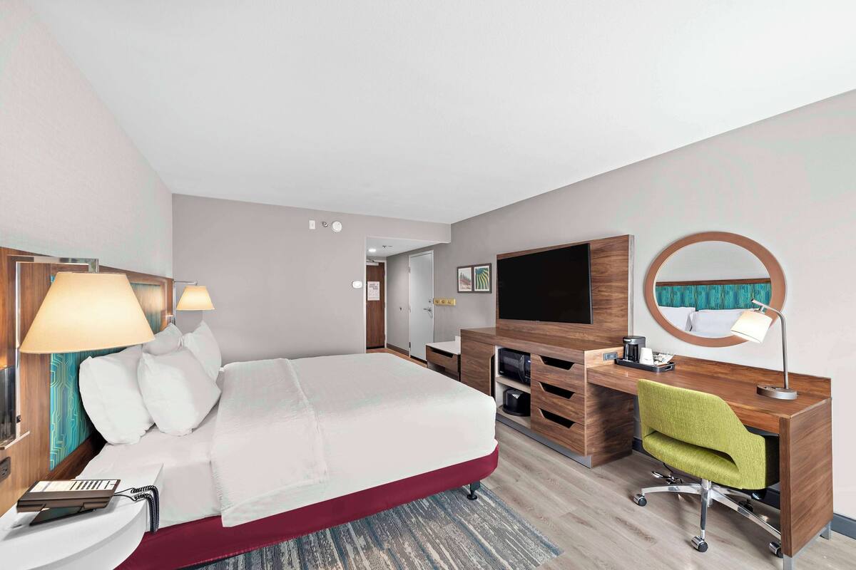 A hotel room with a bed, desk, chair, TV, and a mirror.