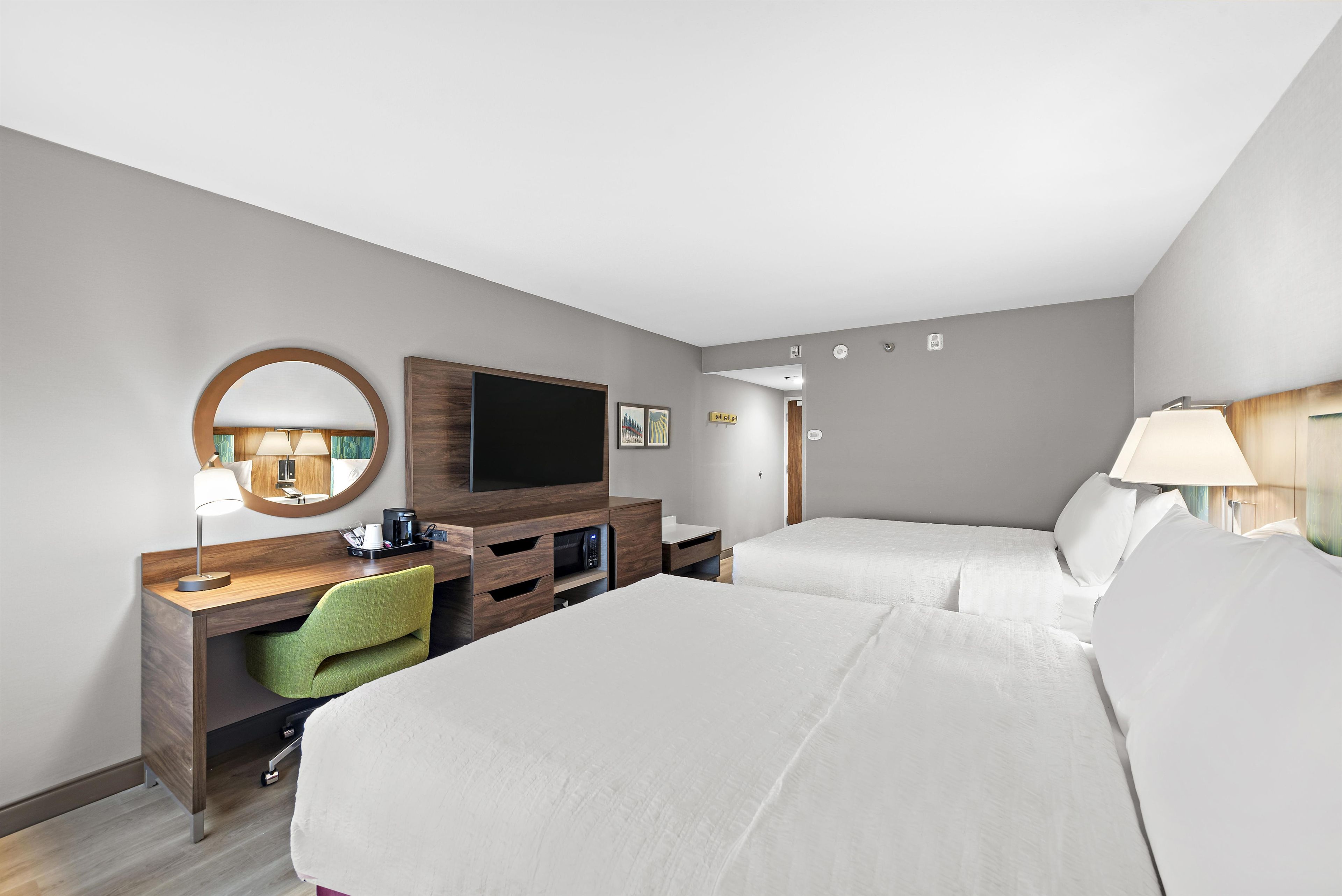 A hotel room with two beds, a desk with a chair, a television, and a mirror.