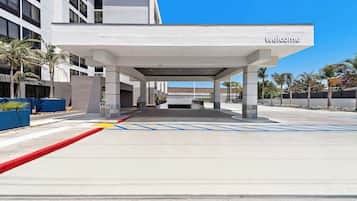Un edificio moderno con un letrero que dice 'welcome', un acceso cubierto y marcas azules para accesibilidad en el suelo.