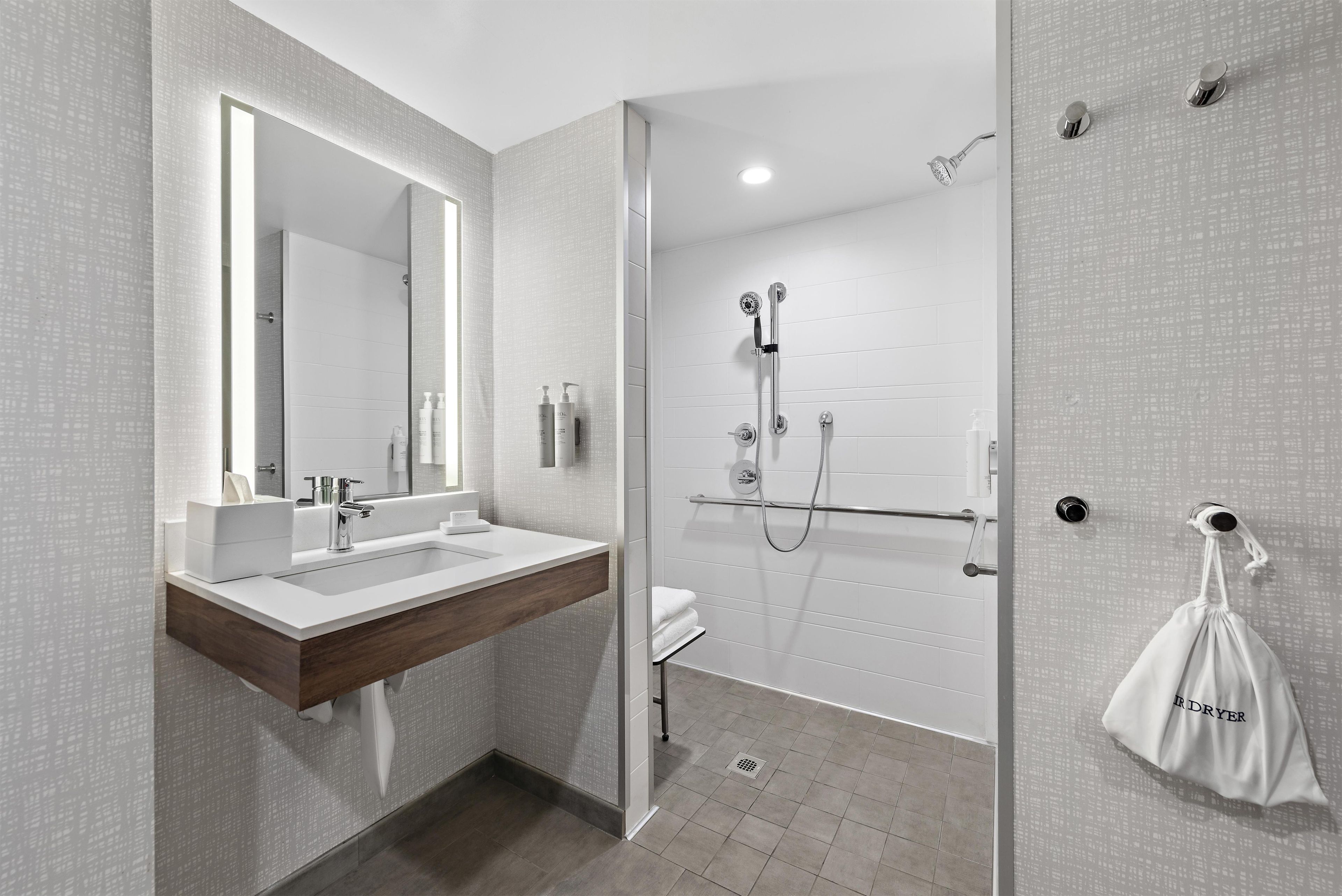 Un baño moderno con un espejo grande, un lavabo, una ducha con cabezal de ducha manual y un perchero para toallas.