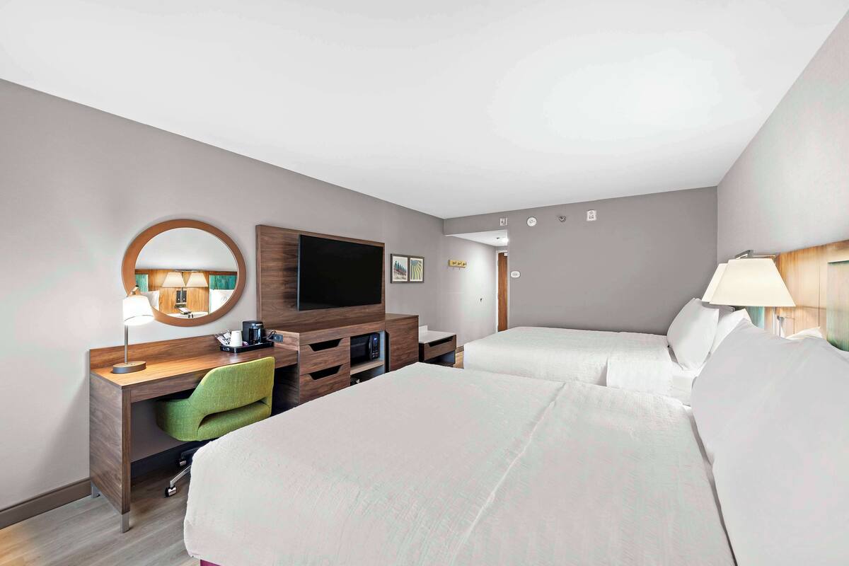 A hotel room with two beds, a desk with a chair, a television, and a mirror.