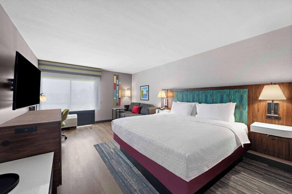 A modern hotel room with a large bed, a desk, a flat-screen TV, and a bathroom with a wooden vanity.