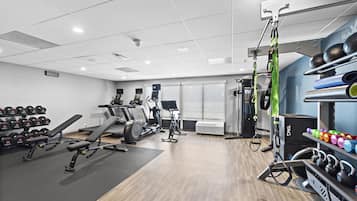 Un gimnasio con equipo de ejercicio, racks de pesas y un aire acondicionado de pared.