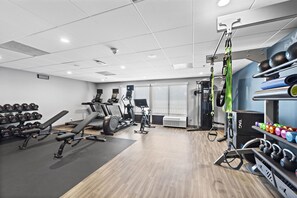 A gym with exercise equipment, weight racks, and a wall-mounted air conditioning unit. - Hampton Inn by Hilton Los Angeles Airport LAX (Inglewood)