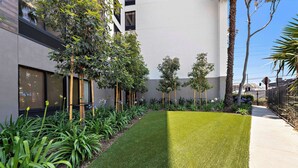 A well-maintained courtyard with a neatly trimmed lawn, various plants, and a modern building with large windows. - Hampton Inn by Hilton Los Angeles Airport LAX (Inglewood)