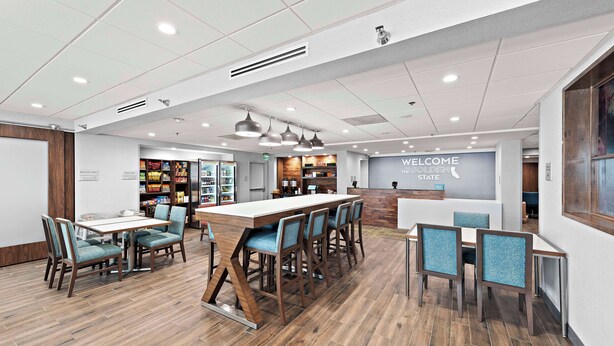 A modern restaurant with a wooden floor, blue upholstered chairs, and a central island. - Hampton Inn by Hilton Los Angeles Airport LAX (Inglewood)