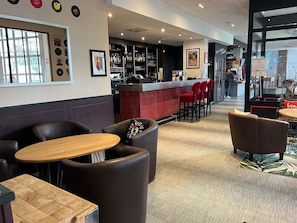 A bar area with a counter, red bar stools, and a seating area with leather chairs and tables. - ibis Paris Nord Villepinte parc des Expositions (Villepinte)