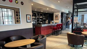 Uma área de bar com balcão, banquetas vermelhas e um espaço de estar com cadeiras de couro e mesas.