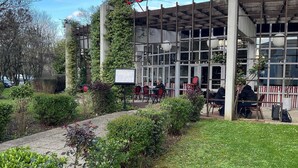 Um edifício com área de estar coberta ao ar livre, um caminho pavimentado e vegetação.