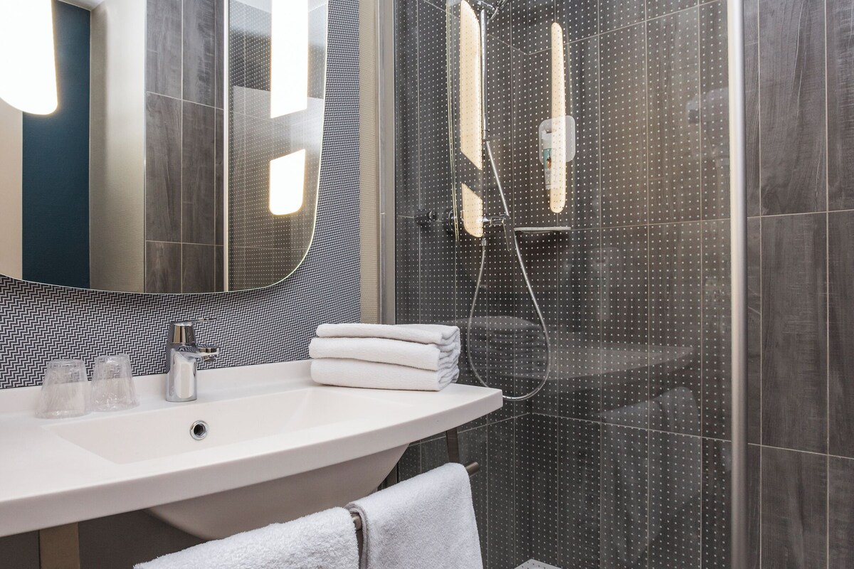 A modern bathroom with a large mirror, a sink, a shower enclosure, and a towel rack.