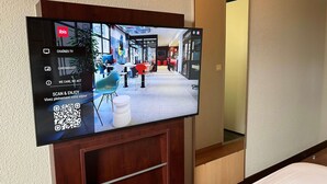 Quarto de hotel com televisão de tela plana presa a um armário de madeira, exibindo um código QR e opções para canais de TV e Chromecast.