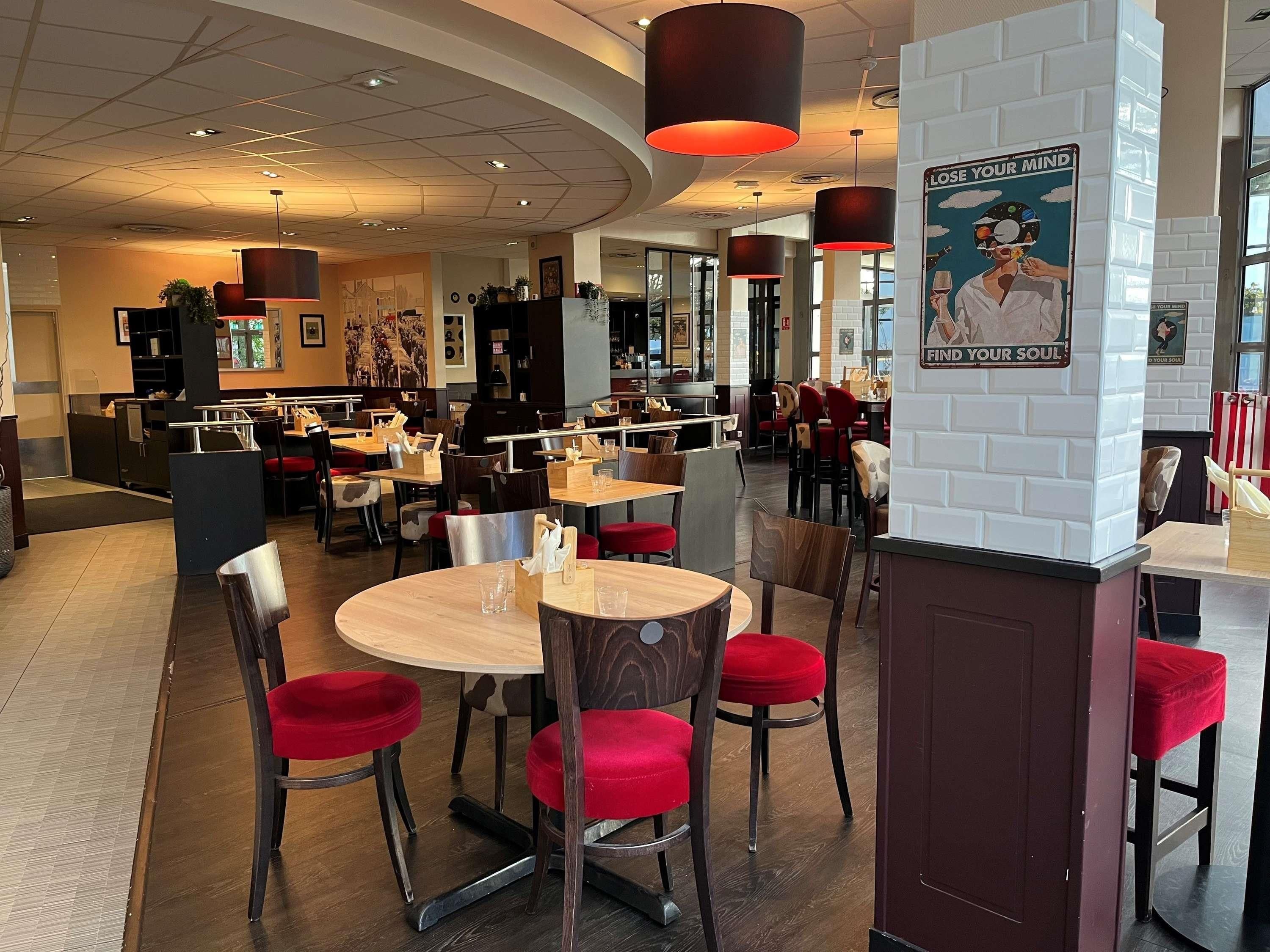 Een restaurant met ronde tafels, rode stoelen en een witte bakstenen muur met motiverende posters.