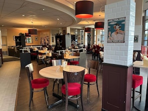 A restaurant with round tables, red chairs, and a white brick wall with motivational posters. - ibis Paris Nord Villepinte parc des Expositions (Villepinte)