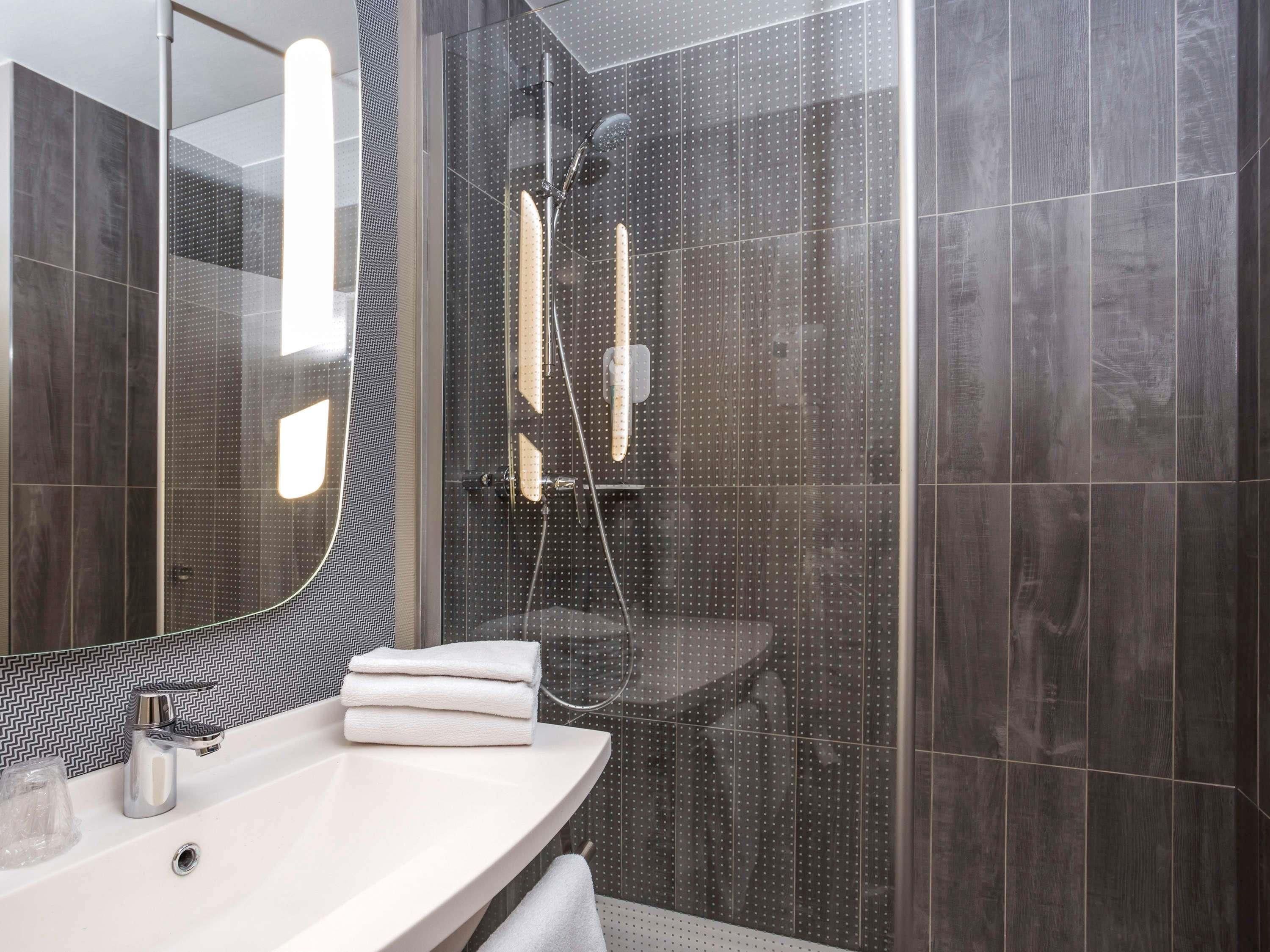 Un baño moderno con ducha de vidrio, lavamanos blanco y espejo con detalles de salpicadero blanco y negro.