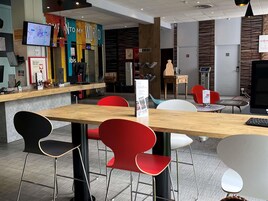 Un interior moderno con un mostrador de recepción de madera, sillas rojas y negras, y un televisor montado en la pared.