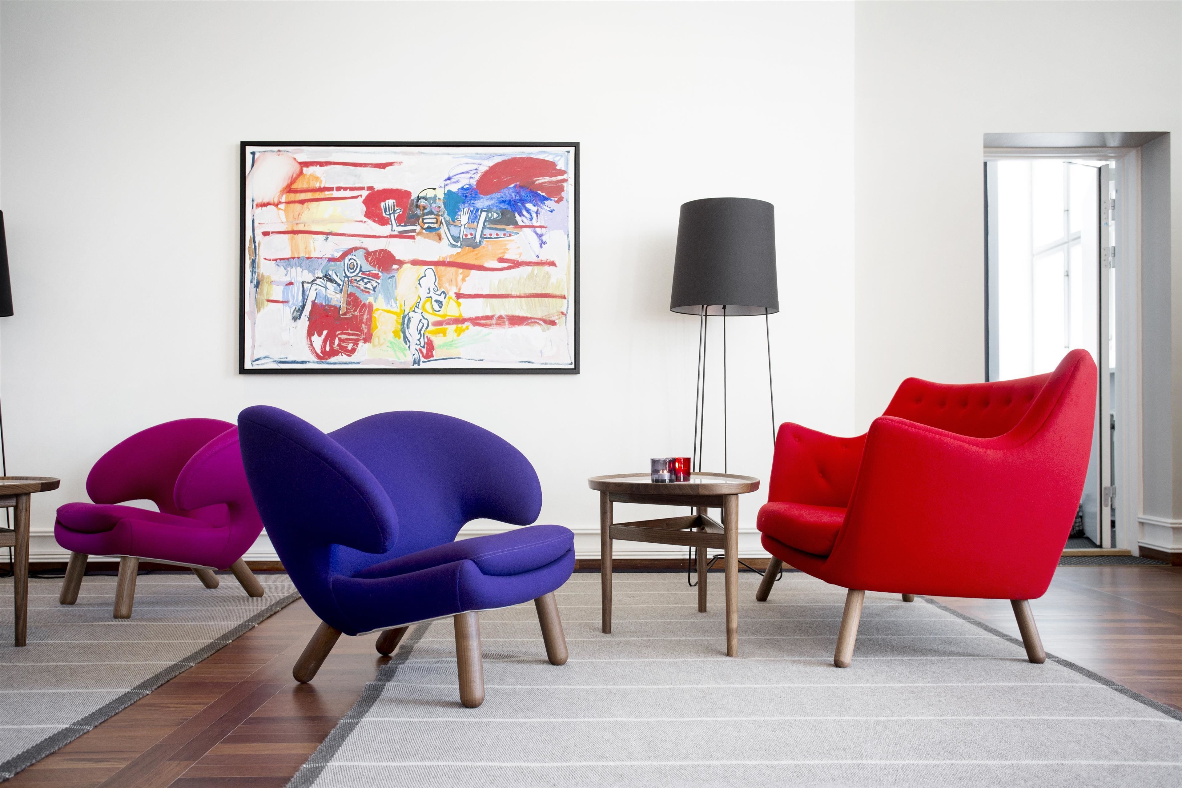 Una habitación moderna con tres sillones llamativos, una lámpara de pie negra y un cuadro abstracto de colores en la pared.
