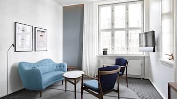 Un salon moderne avec un canapé bleu, une table ronde et deux chaises. On y trouve une fenêtre avec des rideaux, un radiateur et un téléviseur fixé au mur.