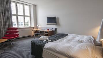 A hotel room with a bed, a desk, a chair, a TV, and a window with curtains.