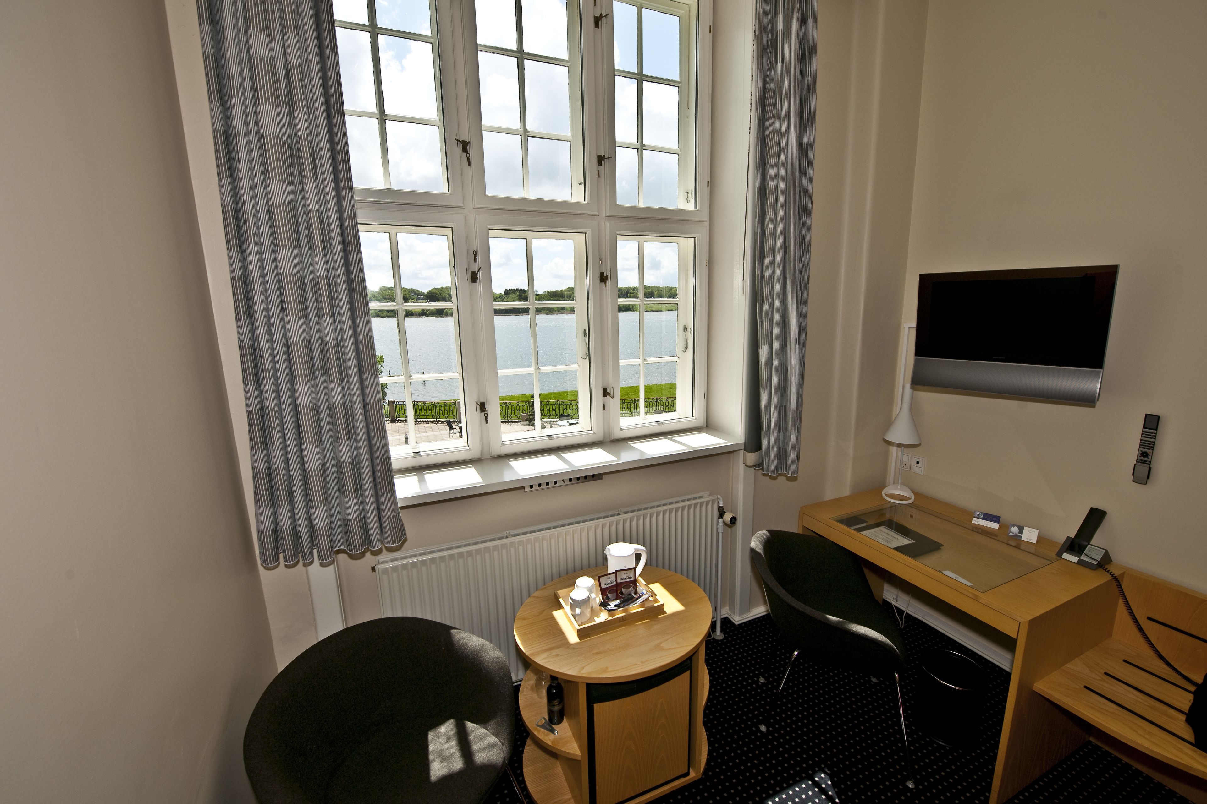 A hotel room with a large window, a desk, a chair, and a TV.
