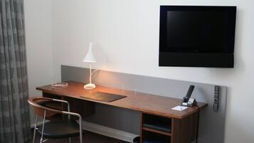 Habitación de hotel con un escritorio de madera, una silla, un televisor montado en la pared y una lámpara.