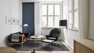 Una sala de estar moderna con un sofá, un sillón, una mesa redonda y un televisor montado en la pared.