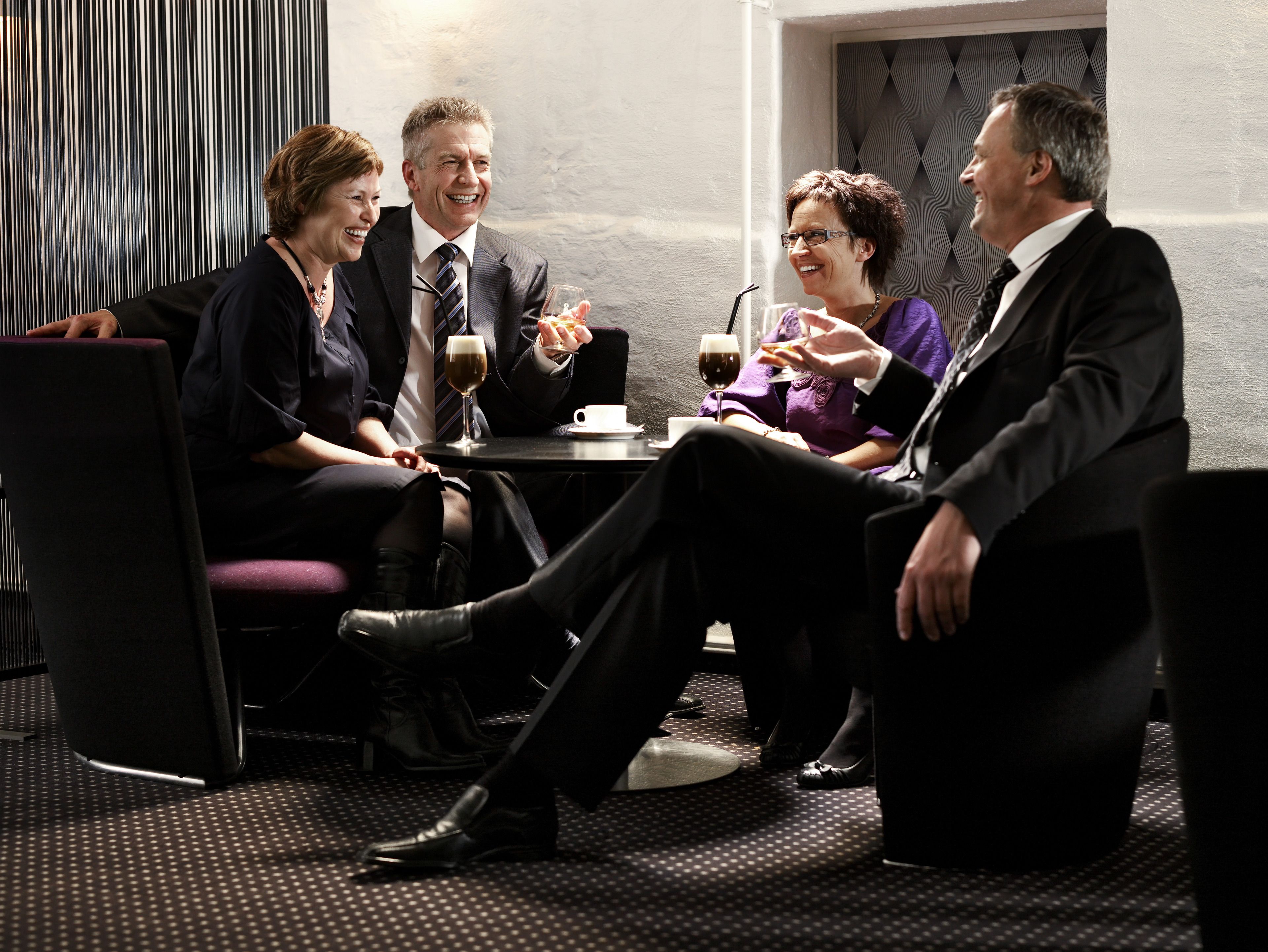 A group of people seated around a table in a modern interior with a patterned floor and a textured wall.