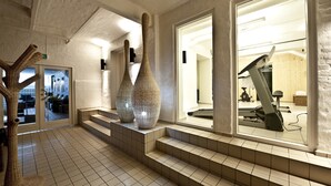 Um hall amplo com piso ladrilhado, escada para um andar superior e grandes vasos decorativos.