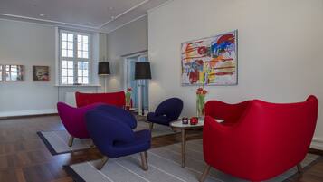 Una sala moderna con sillones rojo y azul, una mesa de centro y un cuadro abstracto grande en la pared.