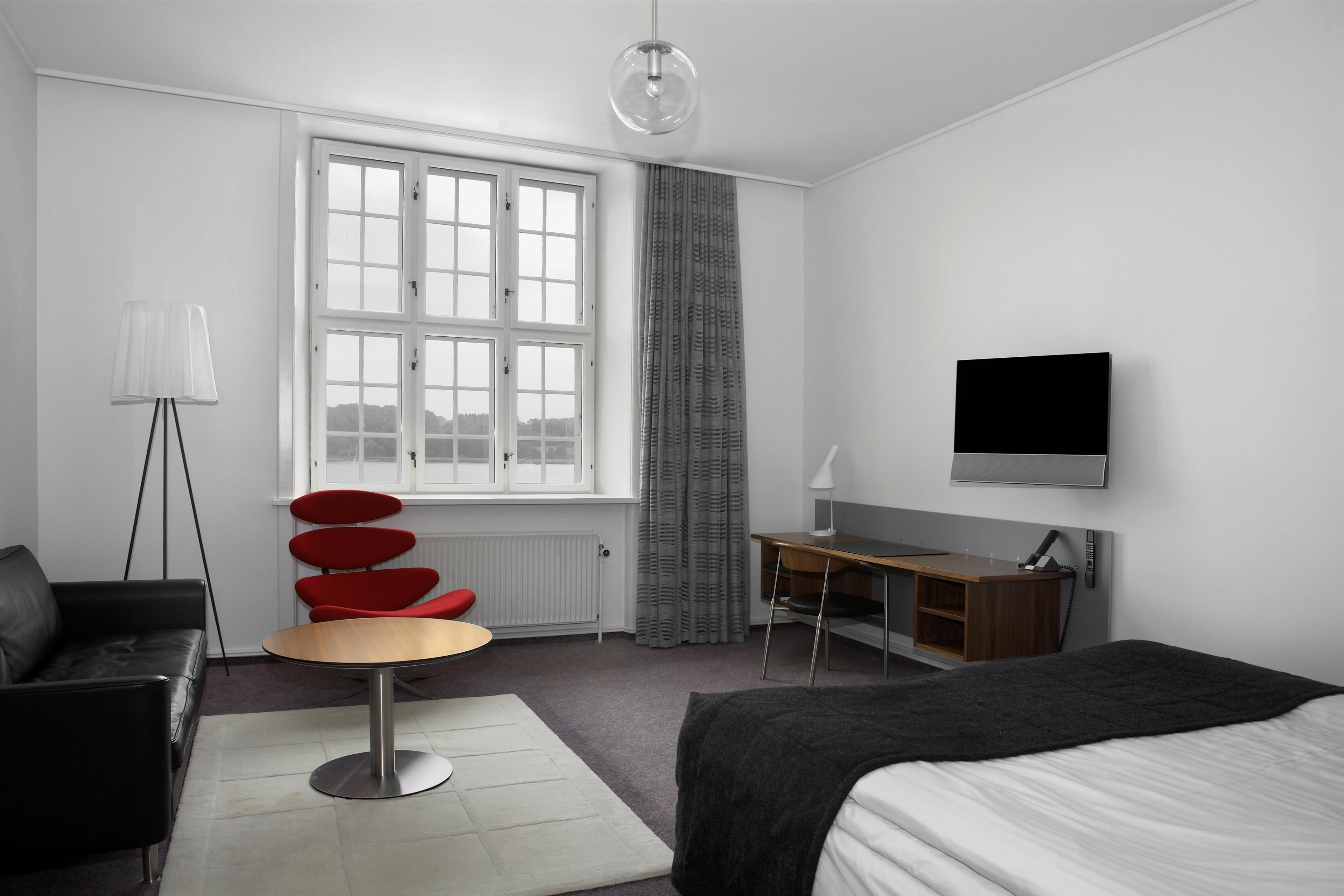 A modern hotel room with a bed, a desk, a chair, a lamp, and a TV.