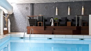 Uma área interna de piscina moderna com piscina transparente, assentos de madeira e iluminação pendente.