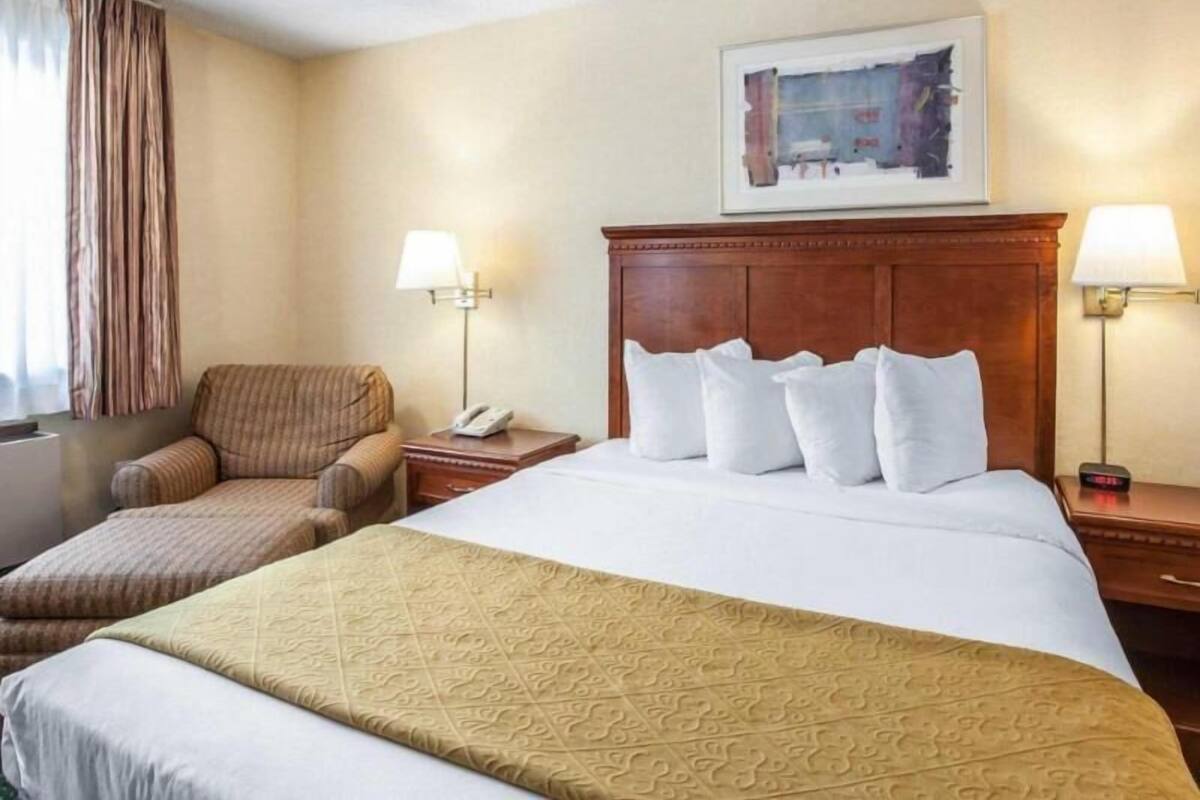 Une chambre d’hôtel avec un grand lit, une chaise, une table de chevet avec une lampe et un tableau au mur.