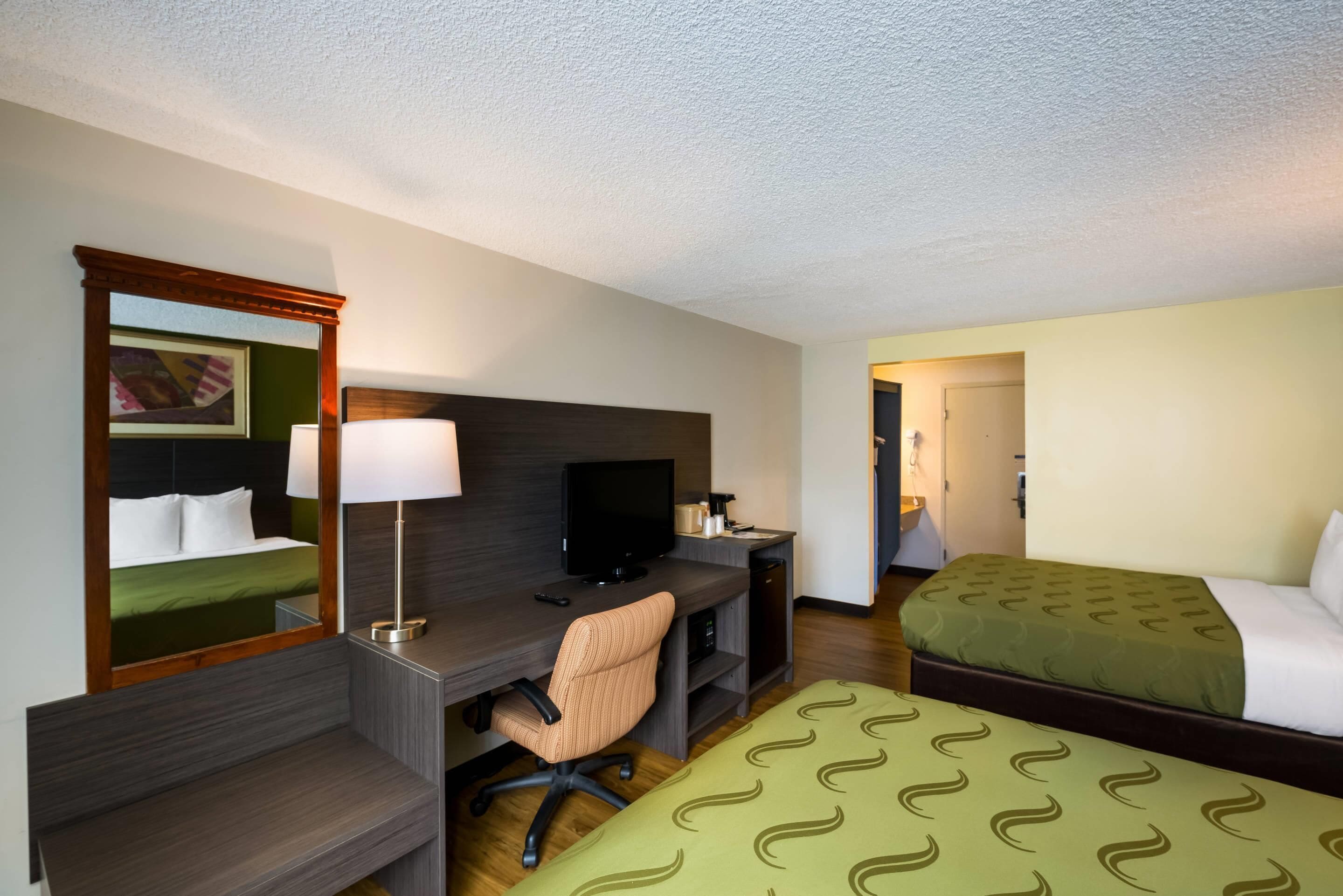 A hotel room with a bed, a desk with a computer, a chair, a TV, and a mirror.