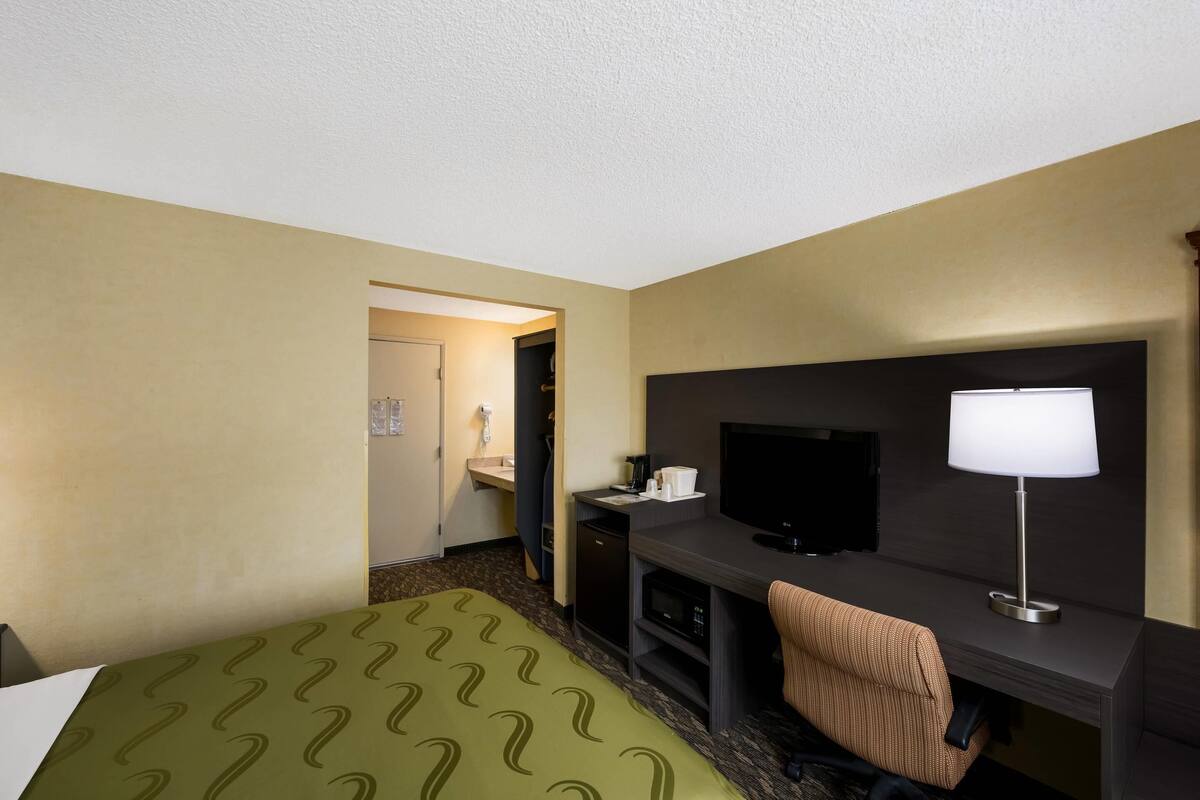 Une chambre d’hôtel avec un lit, un bureau, une télévision et une salle de bain, le tout visible à travers une porte ouverte.