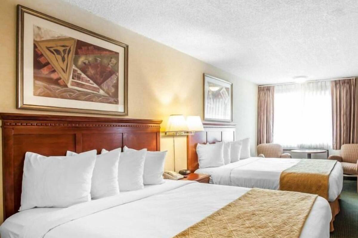 Une chambre d’hôtel avec deux lits, une tête de lit en bois, un tableau au mur, une lampe et une fenêtre avec des rideaux.
