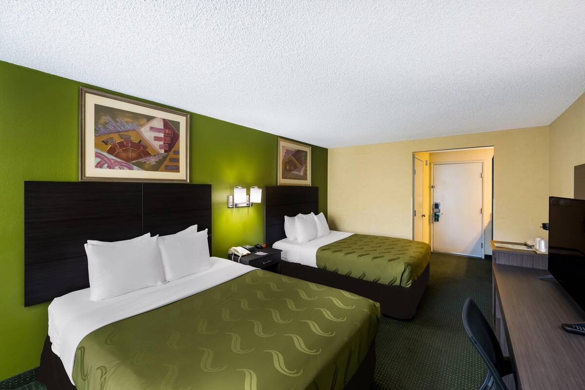 Une chambre d’hôtel avec deux lits, des murs verts, un tableau, un bureau et une télévision.