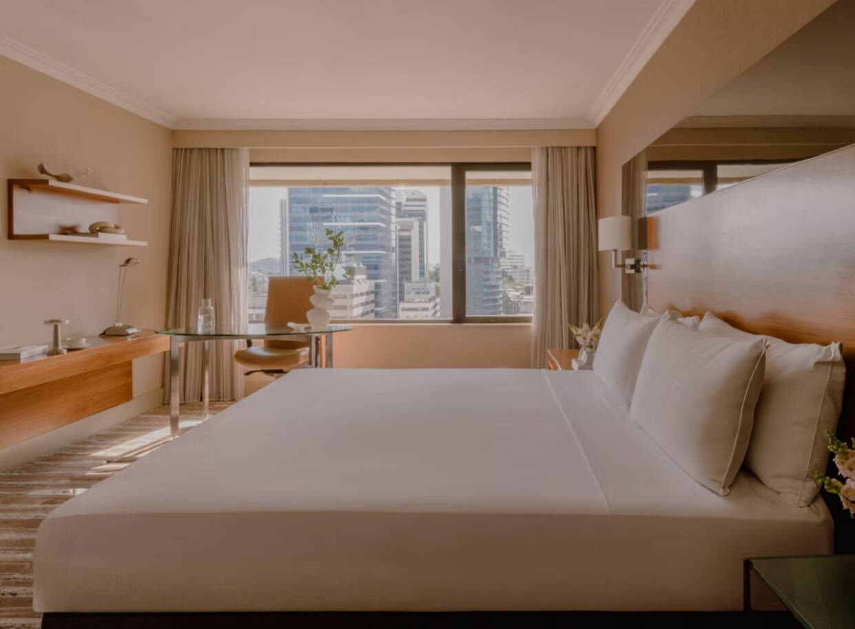 Habitación de hotel con una cama grande, un escritorio, una silla, una mesita y vistas a la ciudad.