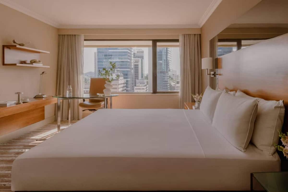 Habitación de hotel con una cama grande, un escritorio, una silla, una mesita y vistas a la ciudad.