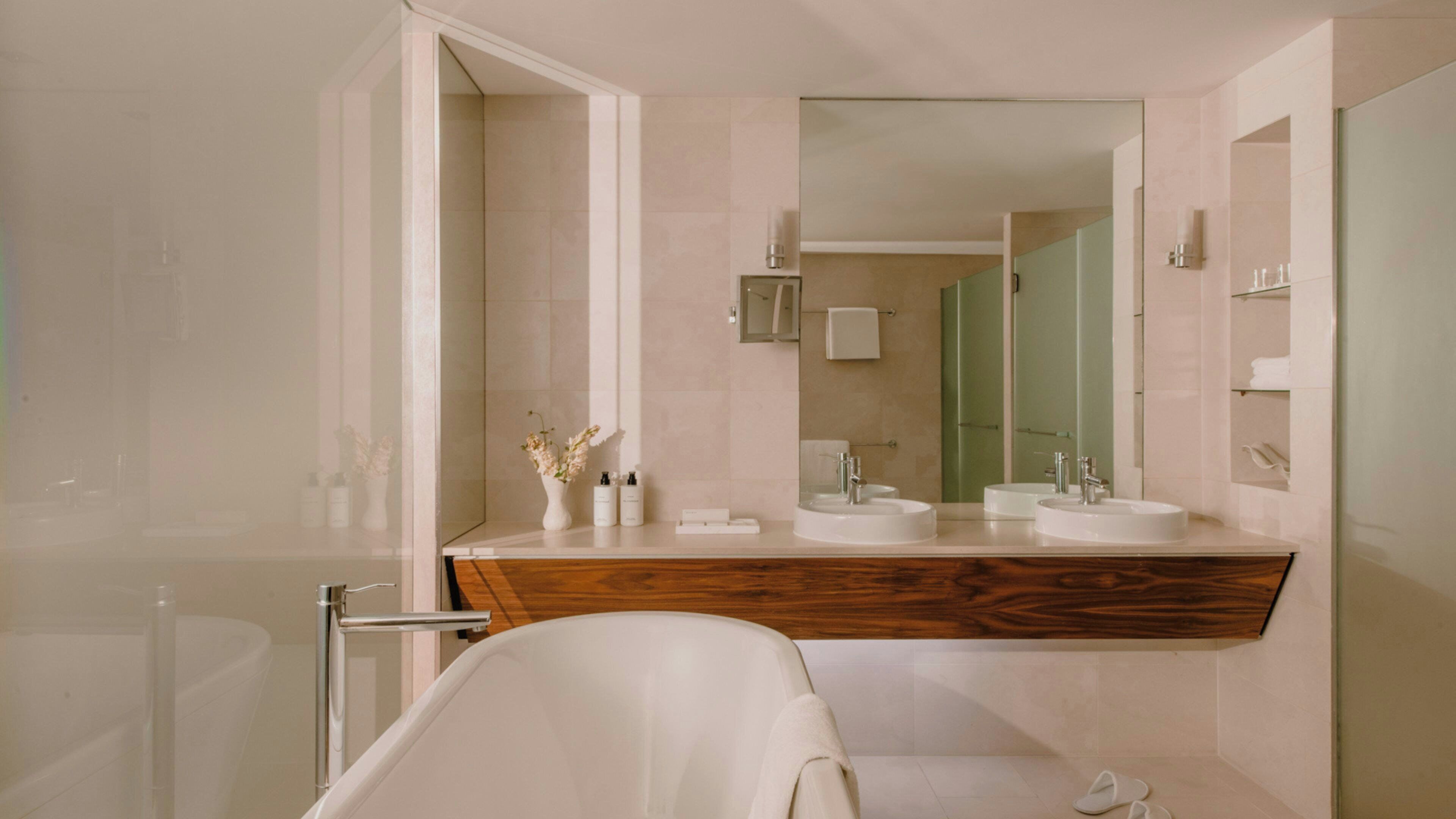 A modern bathroom with a wooden vanity, two sinks, a large mirror, and a bathtub.