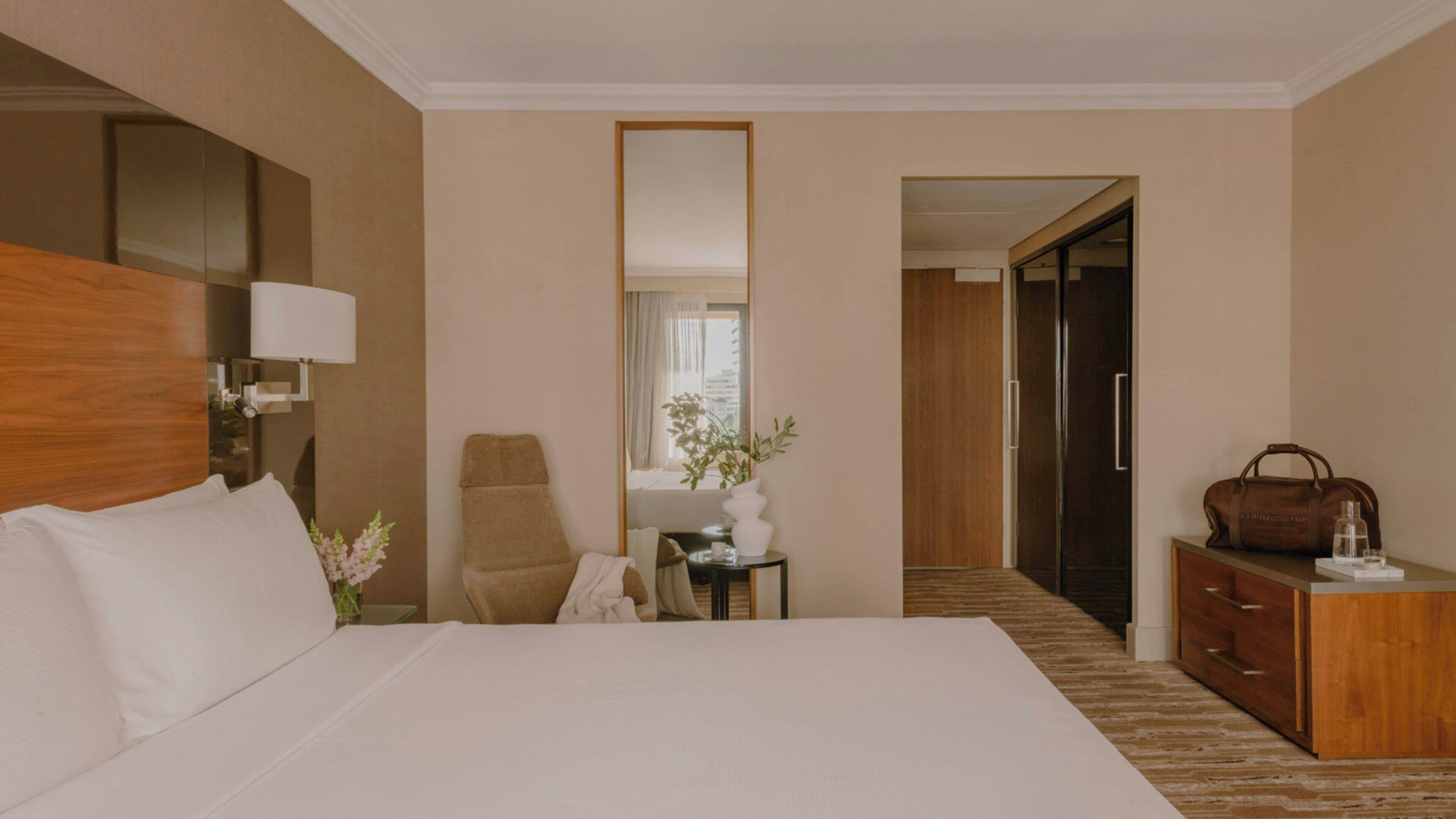 Una habitación de hotel con una cama grande, un escritorio, una silla, un aparador y un espejo.