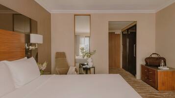 Una habitación de hotel con una cama grande, un escritorio, una silla, un aparador y un espejo.