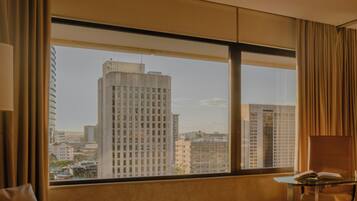 A hotel room with a large window offering a view of high-rise buildings.
