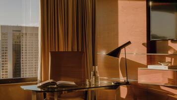 A modern hotel room with a glass table, a book, a lamp, and a view of a cityscape through a window with curtains.
