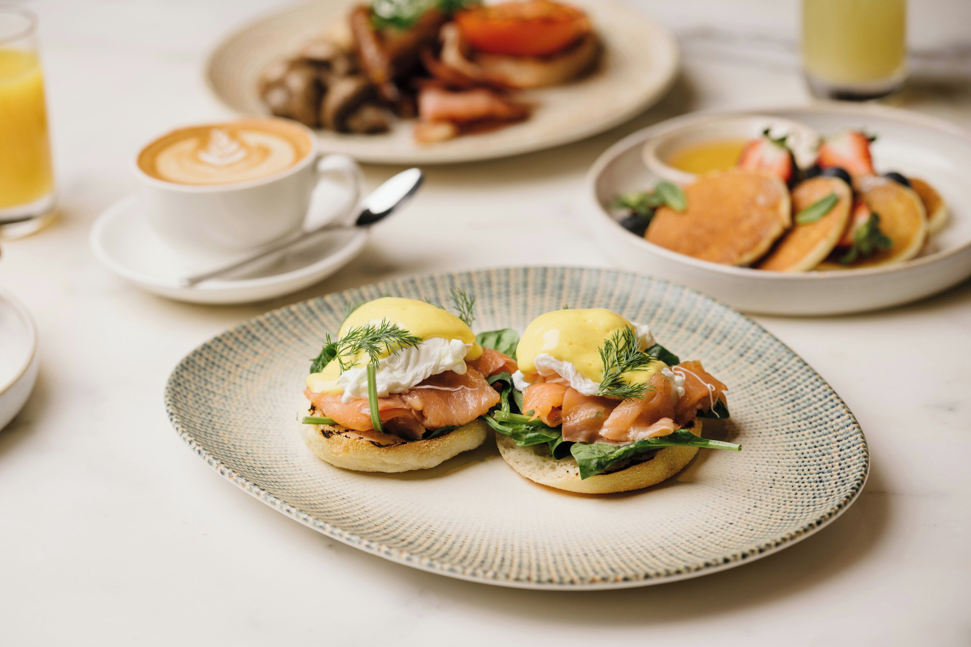 Une table dressée pour le petit-déjeuner avec une assiette d’œufs Bénédicte, une tasse de café et un verre de jus d’orange.