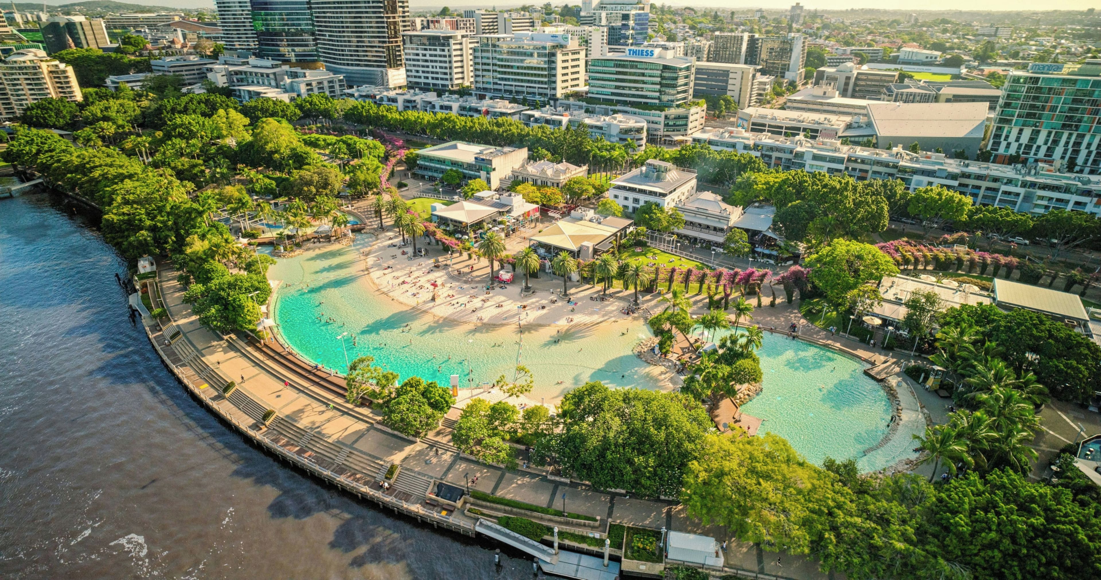 Un complejo turístico frente al mar con una gran piscina, rodeado de exuberante vegetación y edificios modernos.
