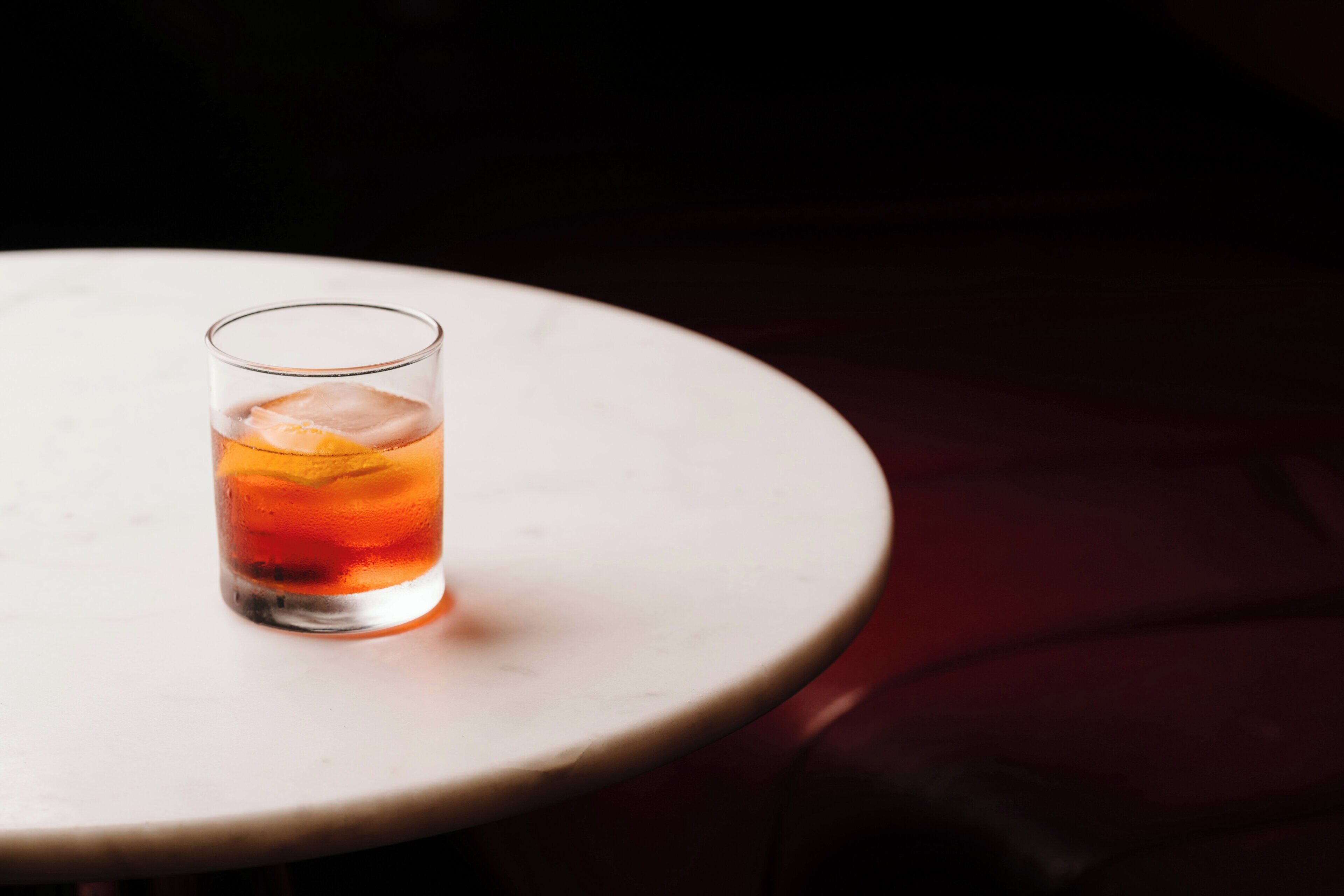 A glass of amber-colored beverage on a white round table.