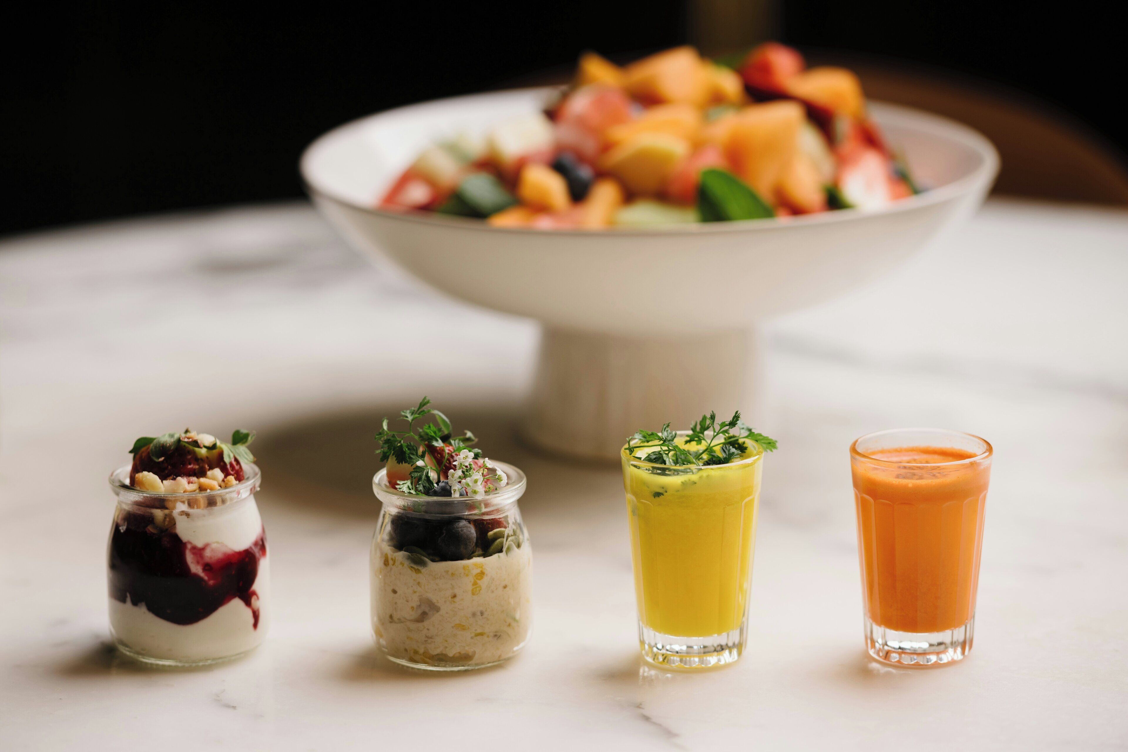 Une table avec un panier de fruits et trois petits verres contenant différentes boissons.