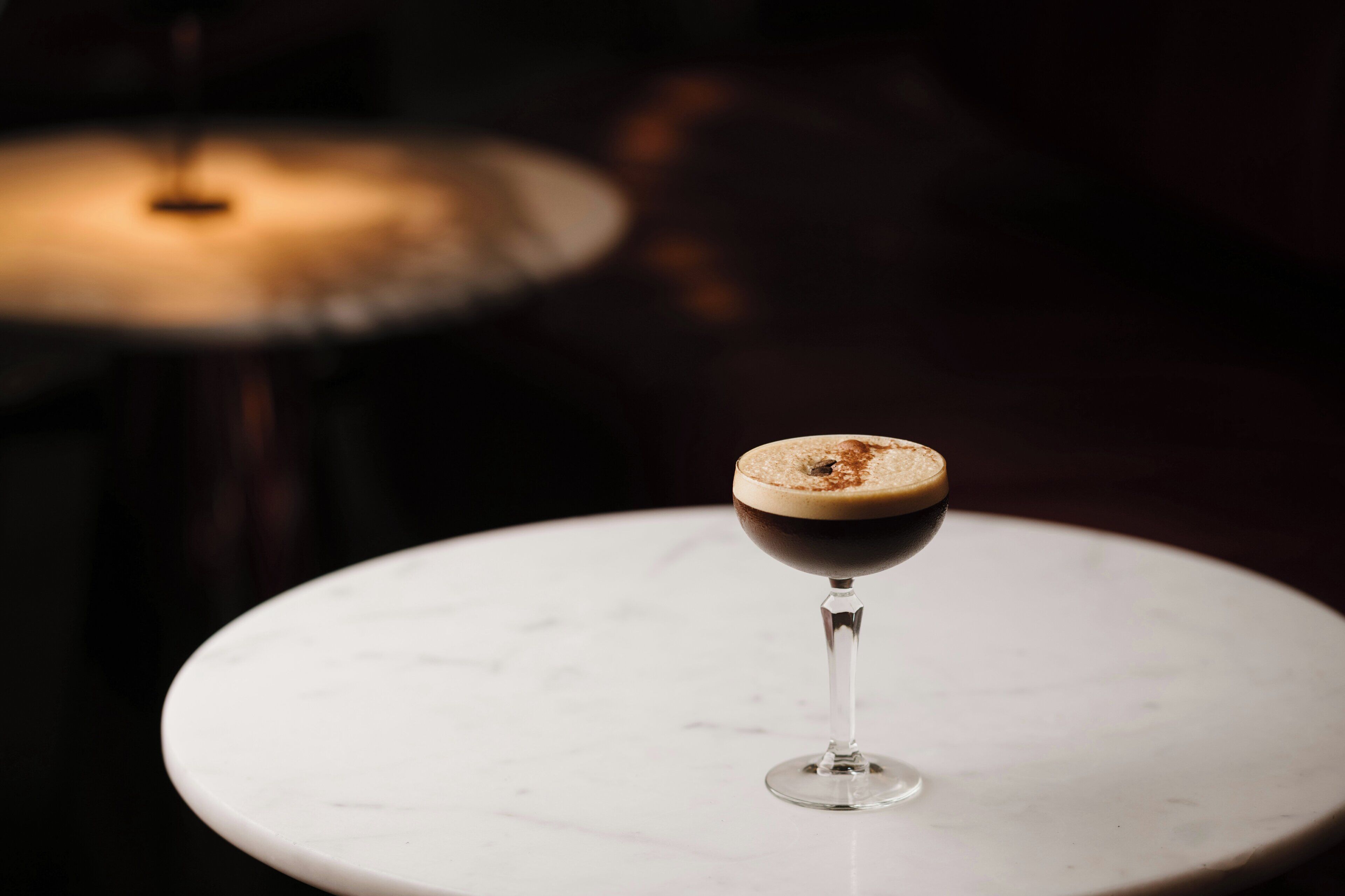 A cocktail in a stemmed glass on a white marble surface.